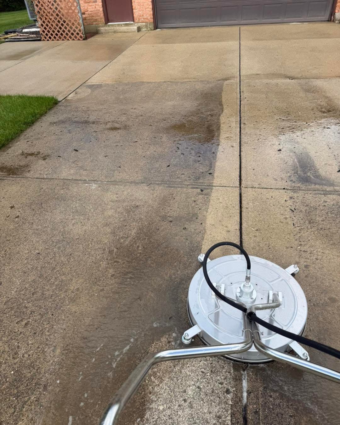 Surface cleaner attachment lifting years of grime off a concrete driveway